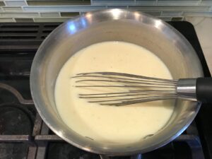 Whisk mixing white sauce in a pot for White Lasagna Recipe with Zucchini and Ground Beef