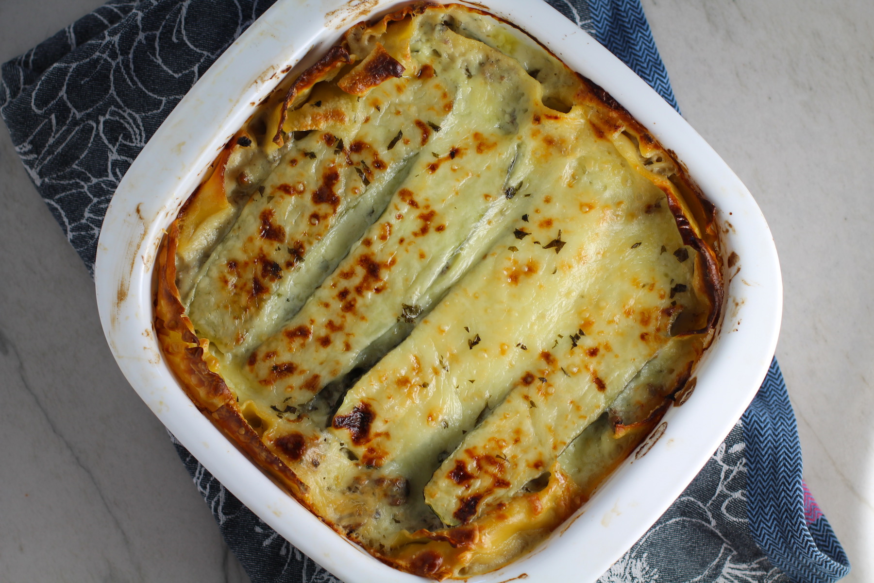 White Lasagna Recipe with Zucchini and Ground Beef with browned melted cheese on top in casserole dish! It's a make-ahead family dinner! It's creamy, hearty, and delicious with layers of noodles, zucchini, ground beef, creamy cheese, and a silky white sauce.