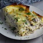 Piece of White Lasagna Recipe with Zucchini and Ground Beef with browned melted cheese on top on a plate with parsley. It's a make-ahead family dinner! It's creamy, hearty, and delicious with layers of noodles, zucchini, ground beef, creamy cheese, and a silky white sauce. 