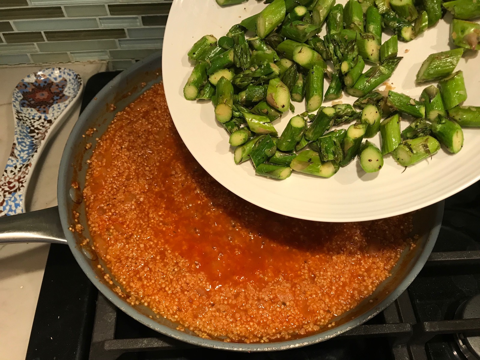 Adding cooked cut asparagus from a plate to risotto in pan for Asparagus and Tomato Quinoa Risotto