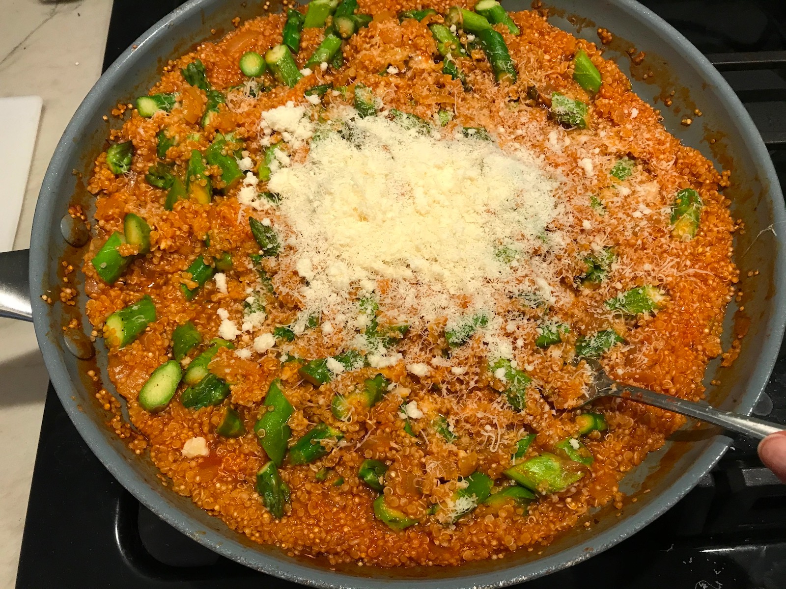 Parmesan cheese added to Asparagus and Tomato Quinoa Risotto in a pan.