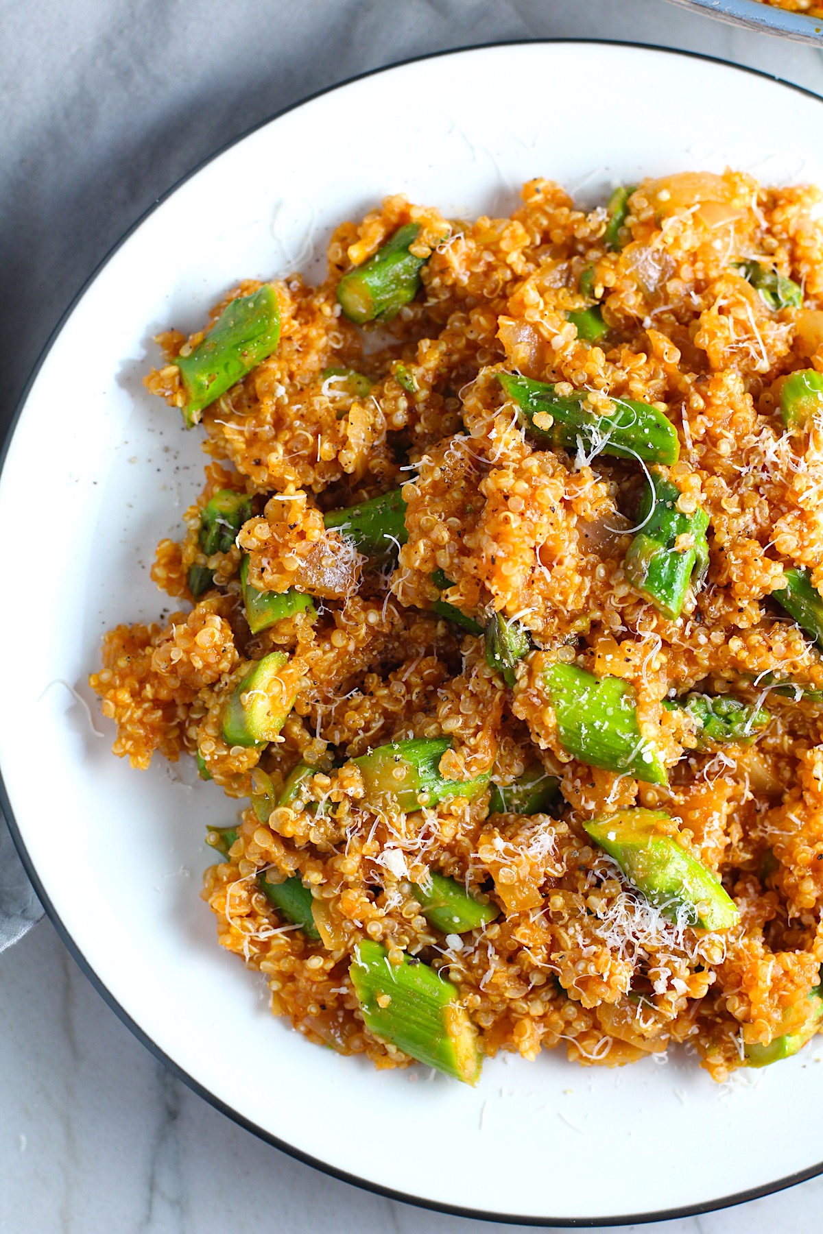 Asparagus and Tomato Quinoa Risotto with parmesan on top on a plate.