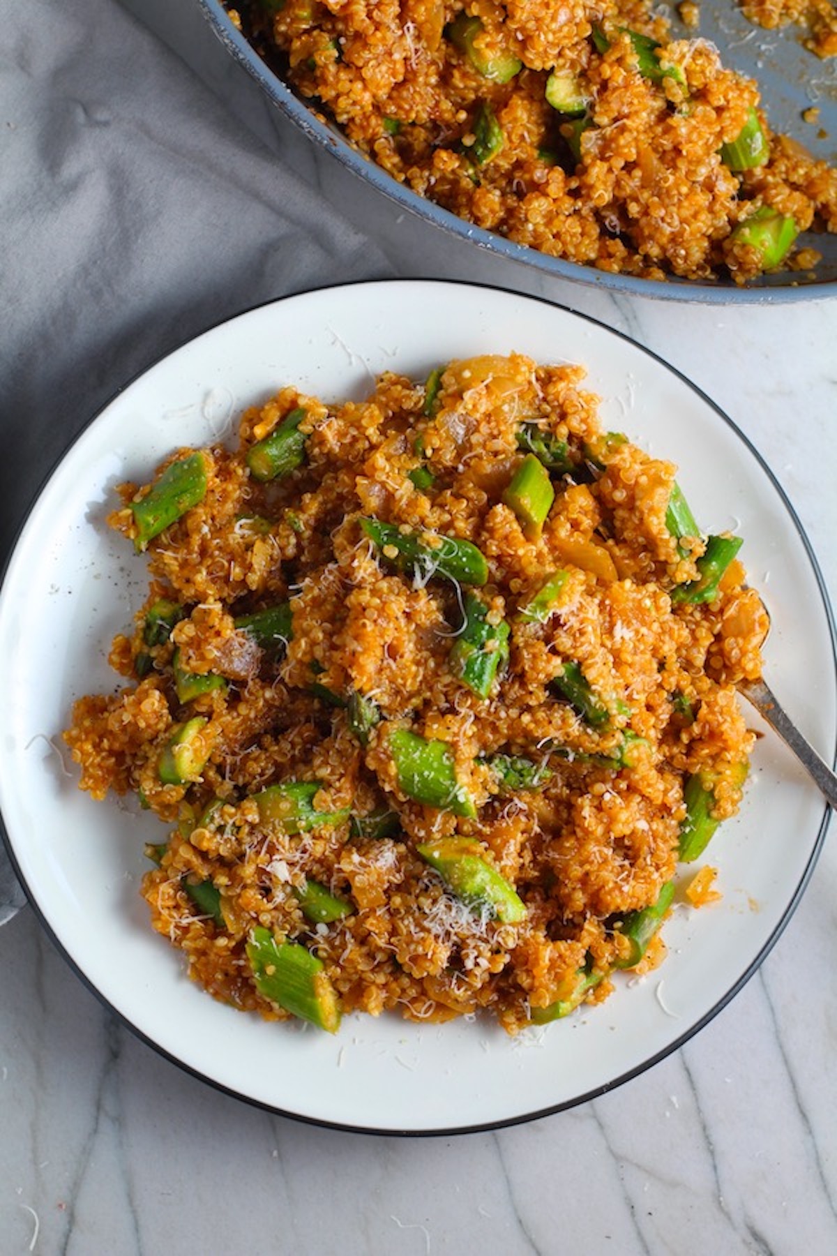 Asparagus and Tomato Quinoa Risotto with parmesan on top on a plate with fork.