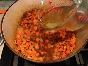 Broth being poured into carrots and onions cooking in pot for Golden Carrot Ginger Soup Recipe.