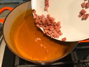 Adding diced ham to creamy carrots for Golden Carrot Ginger Soup Recipe.