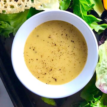 Honey Mustard Salad Dressing Recipe with shallots in a white bowl sitting on a green salad platter with parmesan crisps next to it.