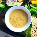 Honey Mustard Salad Dressing Recipe with shallots in a white bowl sitting on a green salad platter with parmesan crisps next to it.
