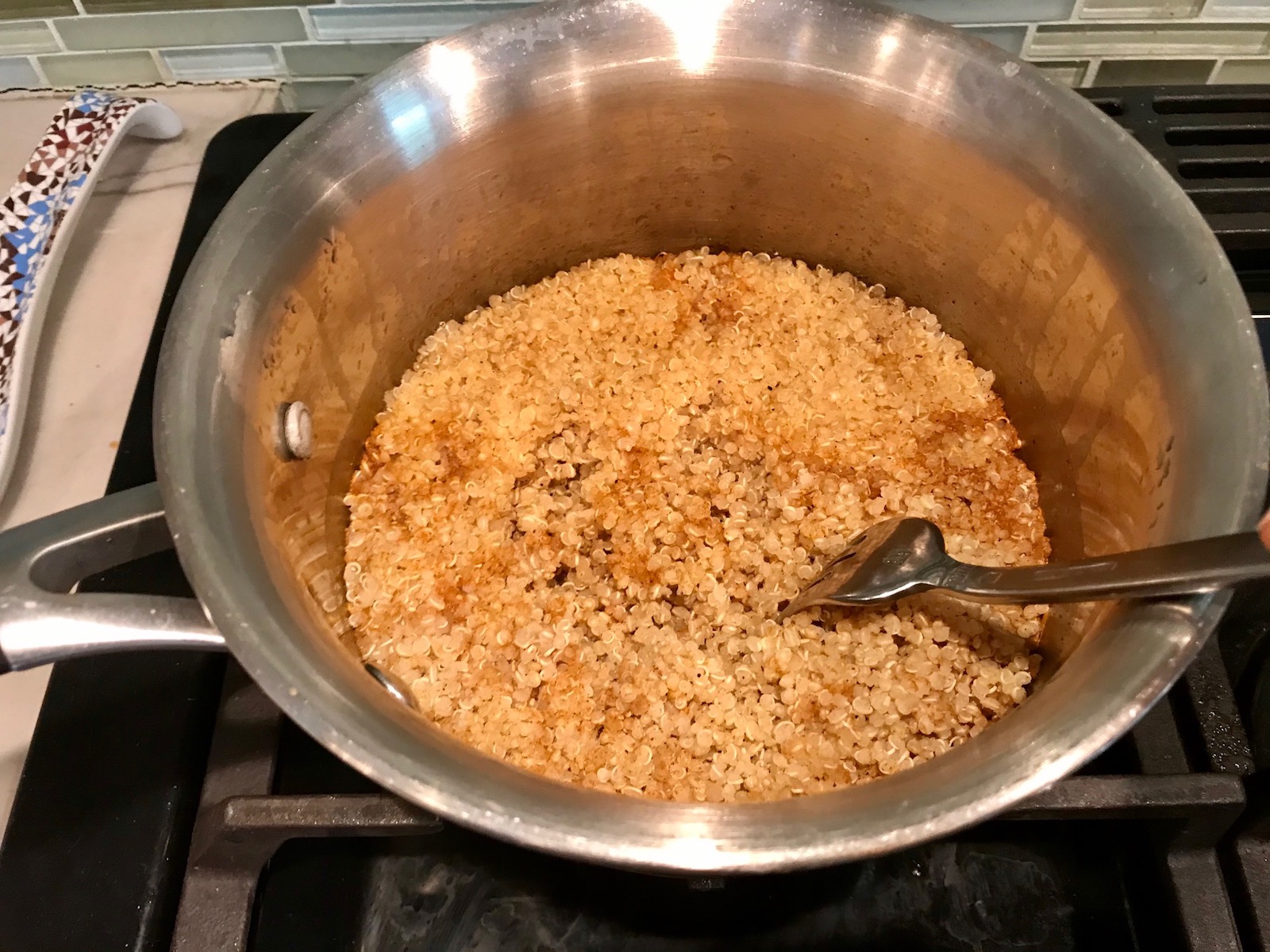 Fork fluffing cooked quinoa in pot for Taco Quinoa Bowl with Ground Beef, corn, cotija cheese, tomatoes, fresh cilantro, and cilantro lime crema