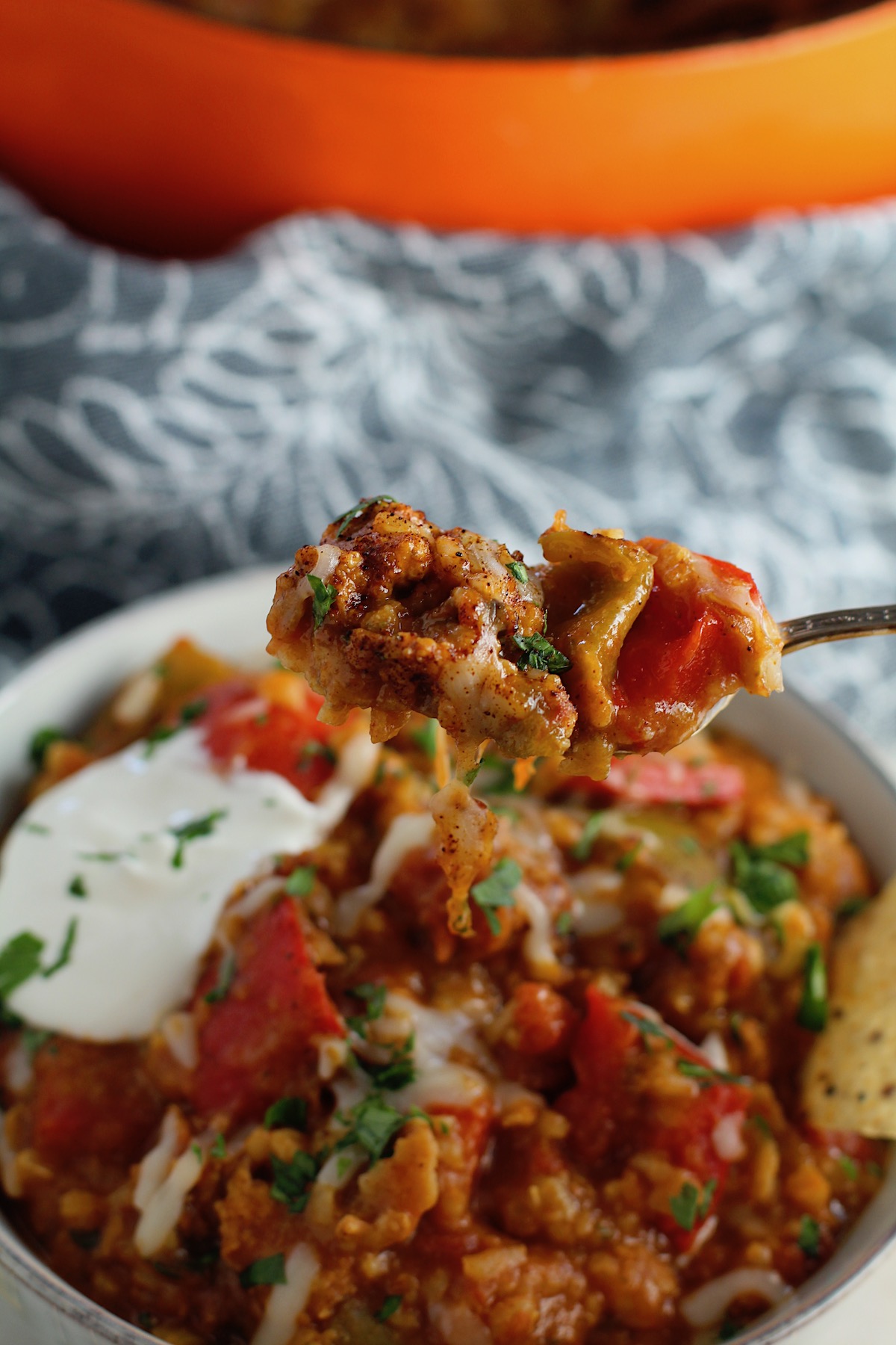 Fork with bite above a bowl of Tex Mex Unstuffed Peppers with Ground Chicken with a dollop of sour cream. Juicy Sweet Bell Peppers are chopped up and cooked with the Tex Mex style ground chicken, tomatoes, Mexican seasonings, cheese, rice and corn tortillas.