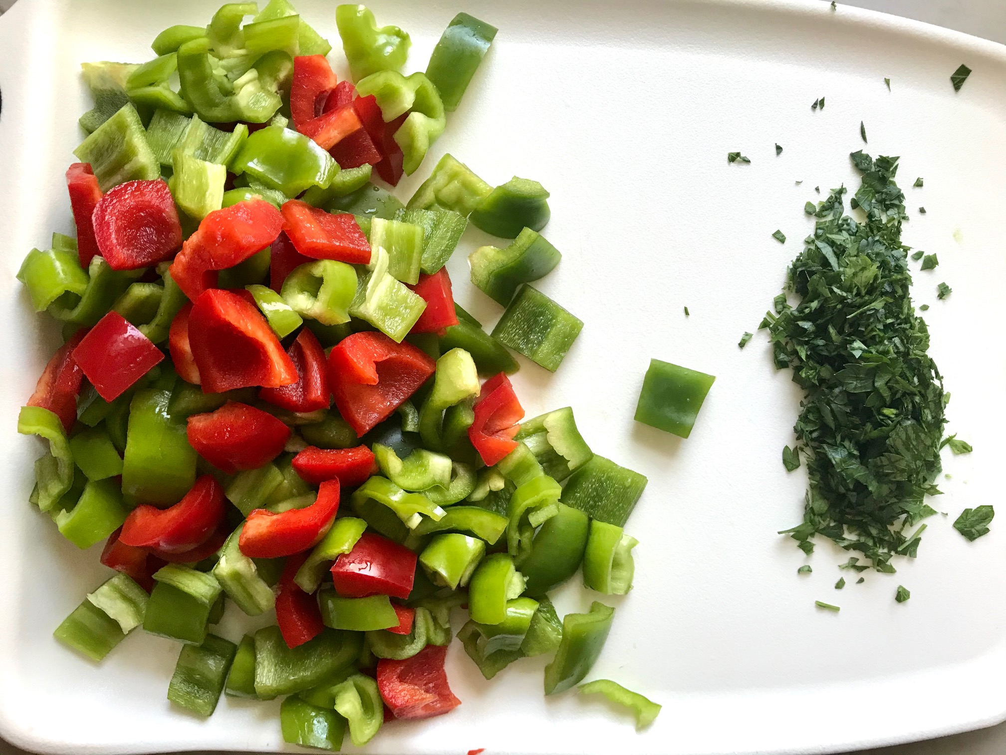 Chopped green and red bell peppers and cilantro on a cutting board for Tex Mex Unstuffed Peppers with Ground Chicken. Juicy Sweet Bell Peppers are chopped up and cooked with the Tex Mex style ground chicken, tomatoes, Mexican seasonings, cheese, rice and corn tortillas.