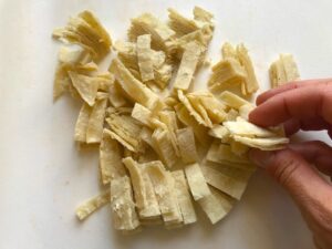 Hand holding tortillas cut into strips for Tex Mex Unstuffed Peppers with Ground Chicken. Juicy Sweet Bell Peppers are chopped up and cooked with the Tex Mex style ground chicken, tomatoes, Mexican seasonings, cheese, rice and corn tortillas.