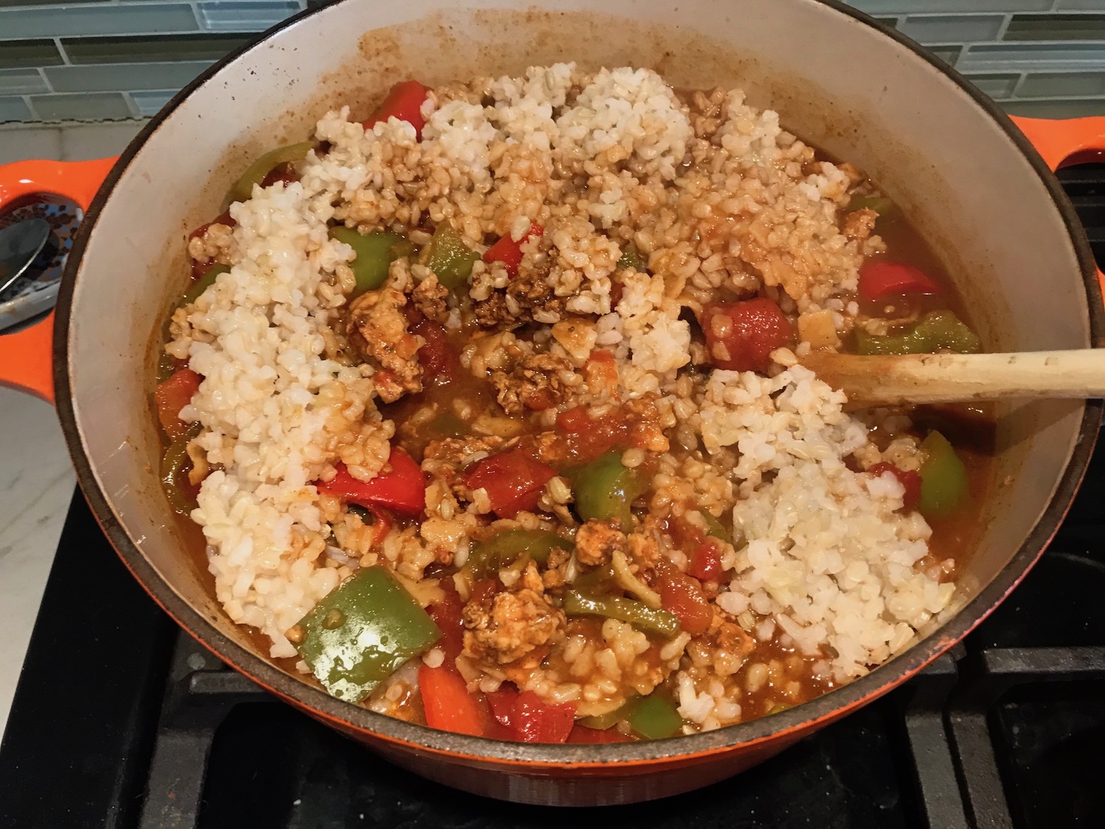 Mixing cooked rice into pot with ground chicken cooking, peppers, and tomatoes for Tex Mex Unstuffed Peppers with Ground Chicken. Juicy Sweet Bell Peppers are chopped up and cooked with the Tex Mex style ground chicken, tomatoes, Mexican seasonings, cheese, rice and corn tortillas.