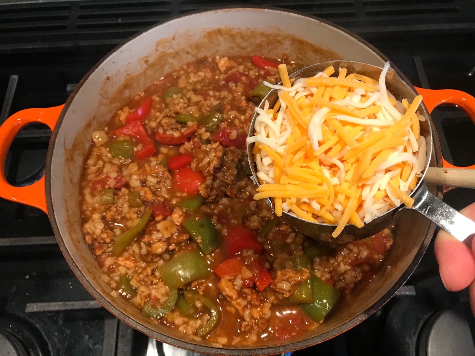 Adding shredded cheese to pot of cooked Tex Mex Unstuffed Peppers with Ground Chicken. Juicy Sweet Bell Peppers are chopped up and cooked with the Tex Mex style ground chicken, tomatoes, Mexican seasonings, cheese, rice and corn tortillas.