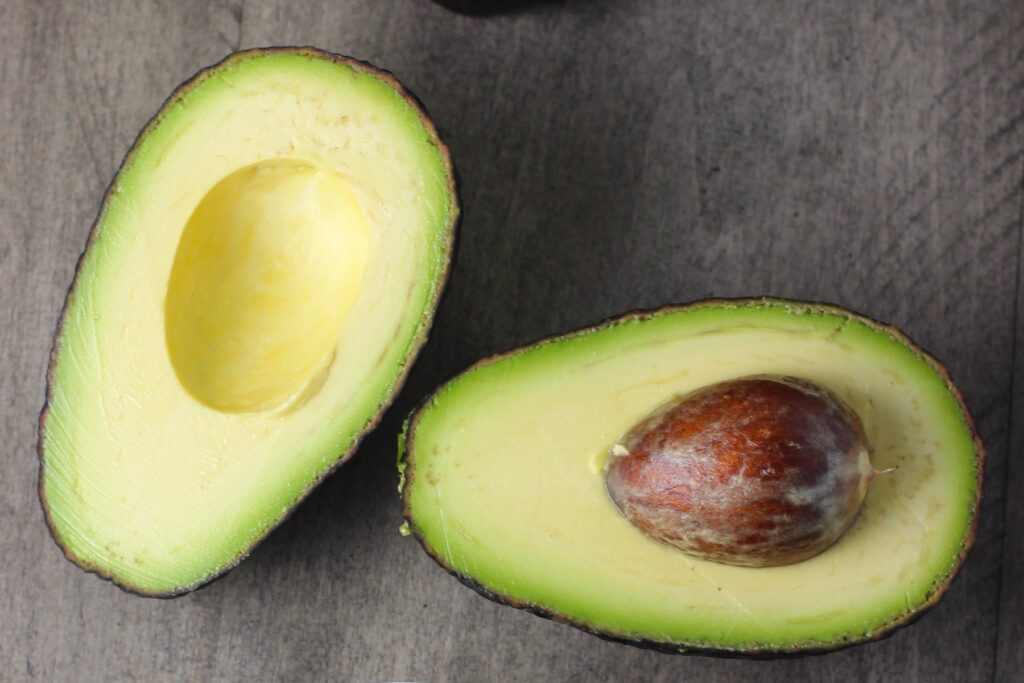 Avocado cut in half on table with pit still in for Avocado Crema Recipe. It goes on everything! It's a creamy, tangy, rich and delicious sauce that's made in just minutes in the blender!