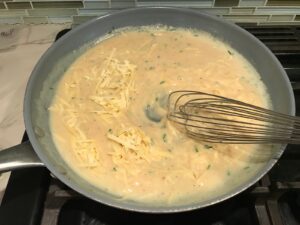 Whisk mixing shredded gruyere cheese into sauce in large frying pan for Velvety Barley Recipe with Bacon and Gruyere Cheese. It's creamy, rich, nutty, smokey, hearty, and utterly delicious.