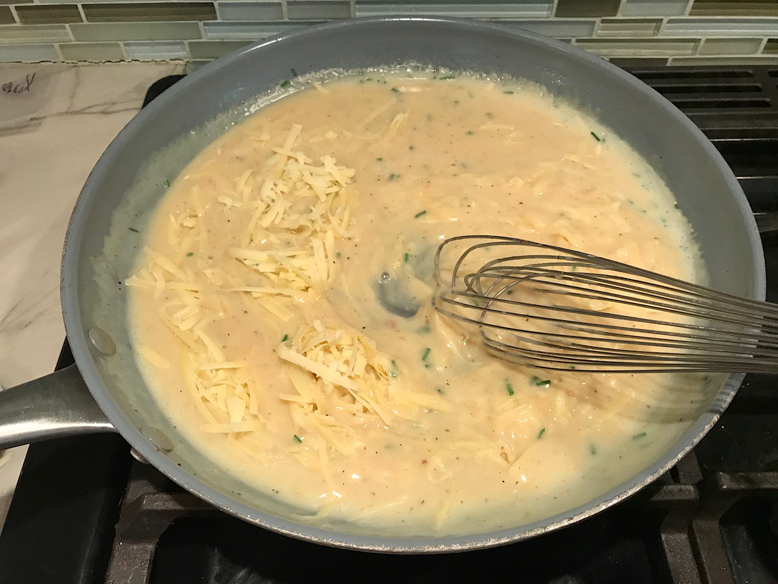 Whisk mixing shredded gruyere cheese into sauce in large frying pan for Velvety Barley Recipe with Bacon and Gruyere Cheese. It's creamy, rich, nutty, smokey, hearty, and utterly delicious.