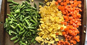 Raw cut asparagus, corn kernels, and sliced carrots on a sheet pan for Creamy Pasta Primavera. It has fettuccine, parmesan cheese, roasted asparagus, carrots, tomatoes and fresh corn kernels.