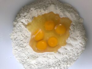 Raw eggs added into the 'well' in the center of the flour for the homemade pasta recipe.