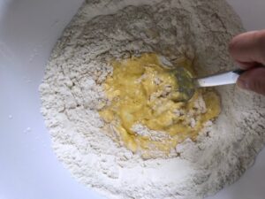 Raw eggs being mixed with a fork into the 'well' in the center of the flour for the homemade pasta recipe.