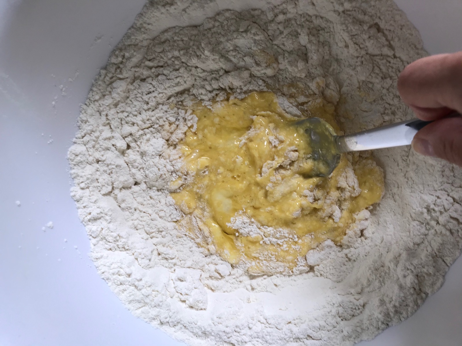 Raw eggs being mixed with a fork into the 'well' in the center of the flour for the homemade pasta recipe.