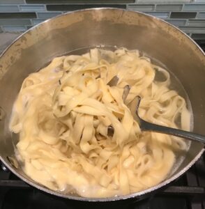 Cooked homemade pasta being lifted up out of the pot with a pasta spoon. being lifted
