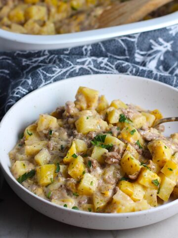 Cheesy Hamburger Potato Casserole in a bowl with a spoon. It's an easy, yummy, and cozy weeknight family dinner.