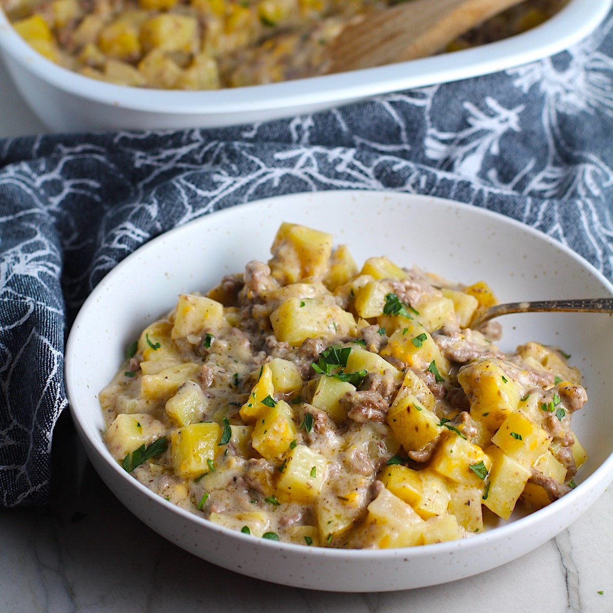 Cheesy Hamburger Potato Casserole in a bowl with a spoon. It's an easy, yummy, and cozy weeknight family dinner.