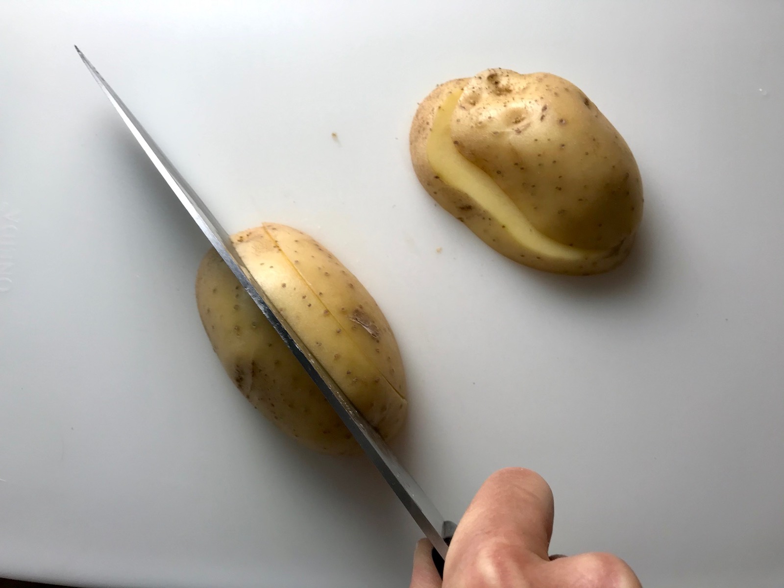 Knife slicing raw yukon gold potato with skin on for Cheesy Hamburger Potato Casserole. It's an easy, yummy, and cozy weeknight family dinner.
