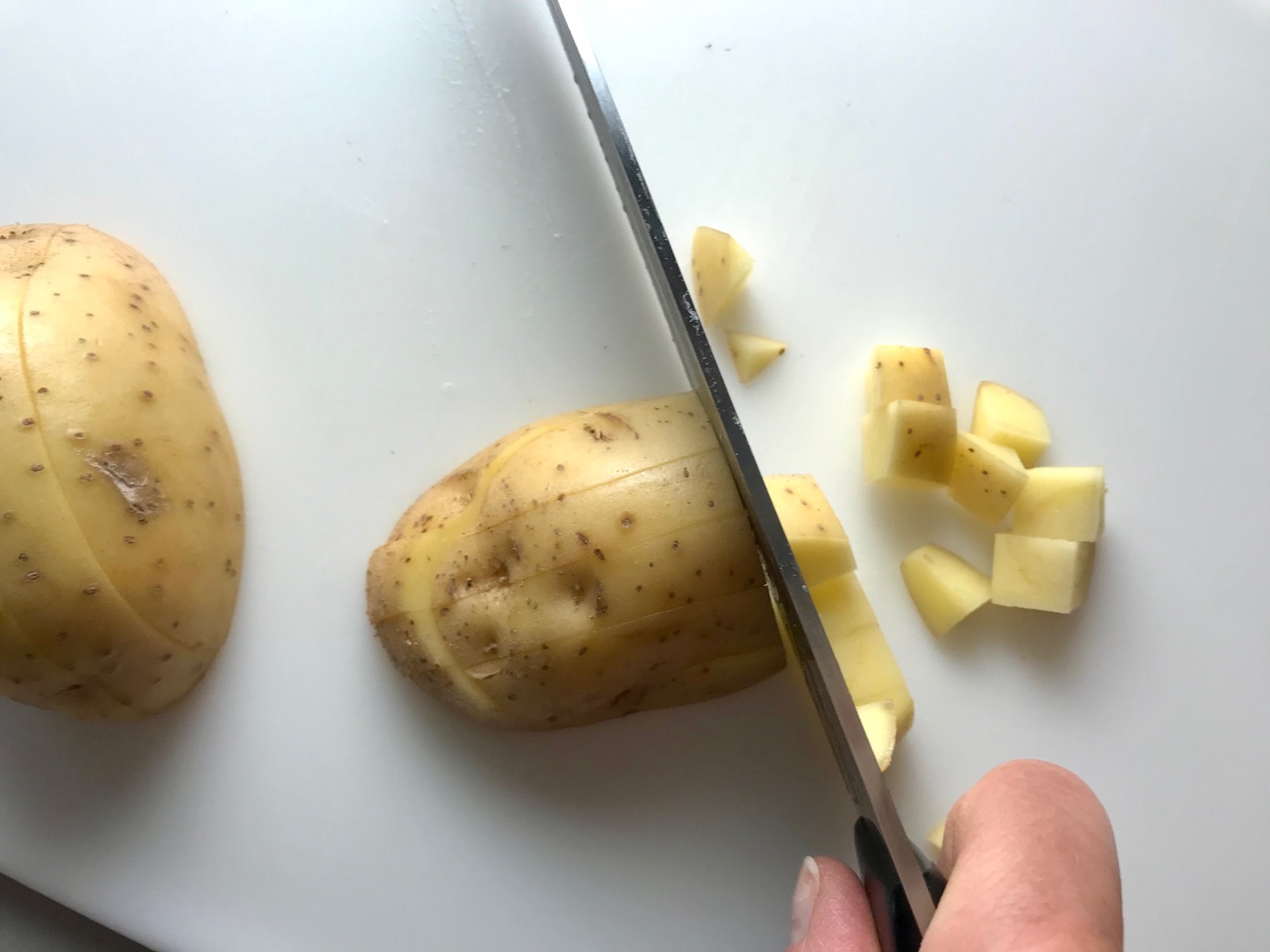 Knife dicing raw yukon gold potato with skin on for Cheesy Hamburger Potato Casserole. It's an easy, yummy, and cozy weeknight family dinner.