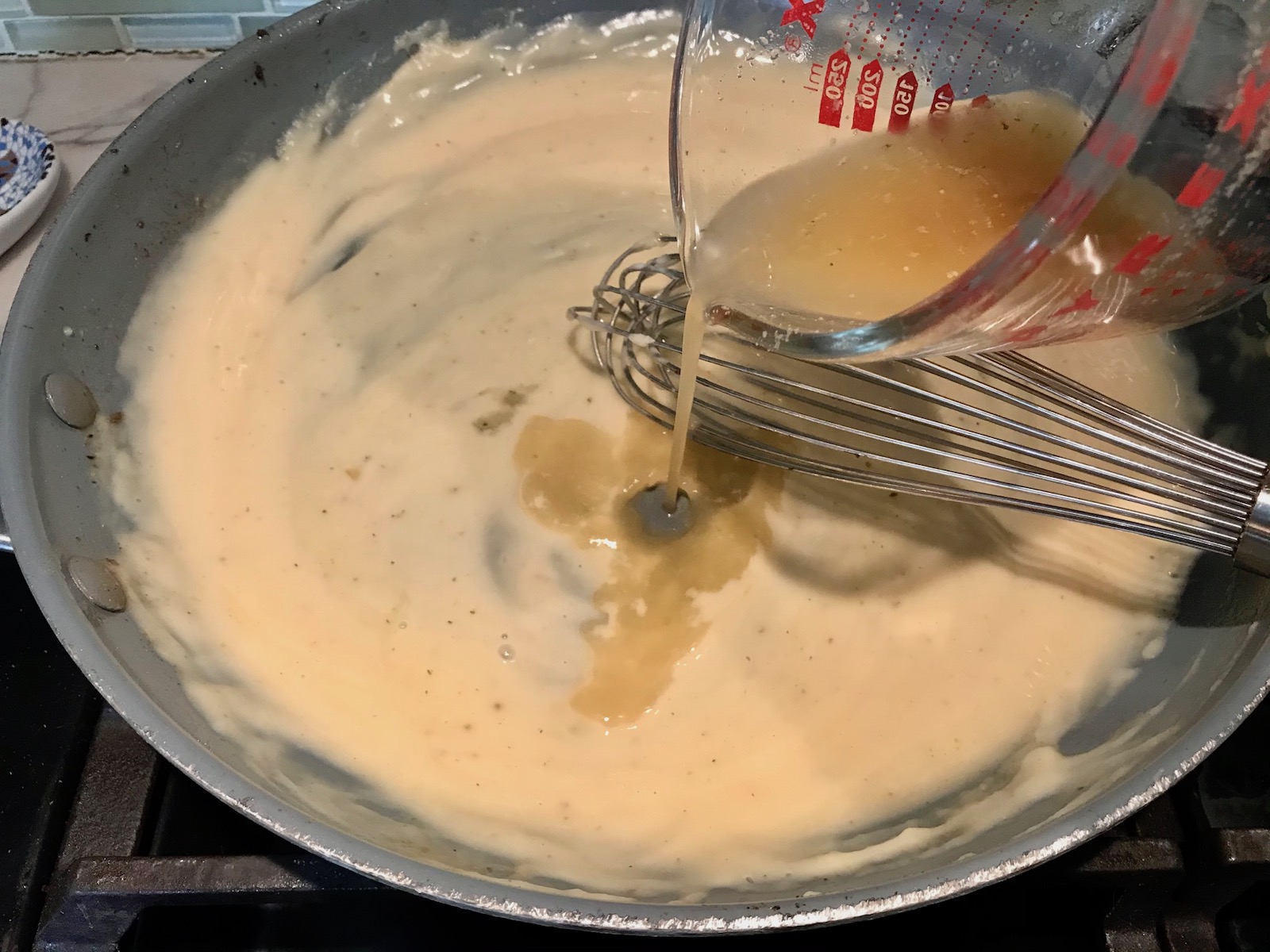 Whisking broth into the roux for Cheesy Hamburger Potato Casserole. It's an easy, yummy, and cozy weeknight family dinner.