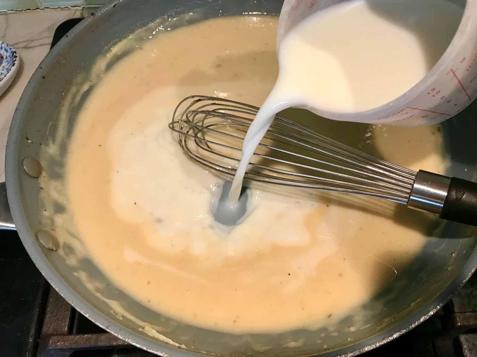 Whisking the milk into the sauce in the pan for Cheesy Hamburger Potato Casserole. It's an easy, yummy, and cozy weeknight family dinner.