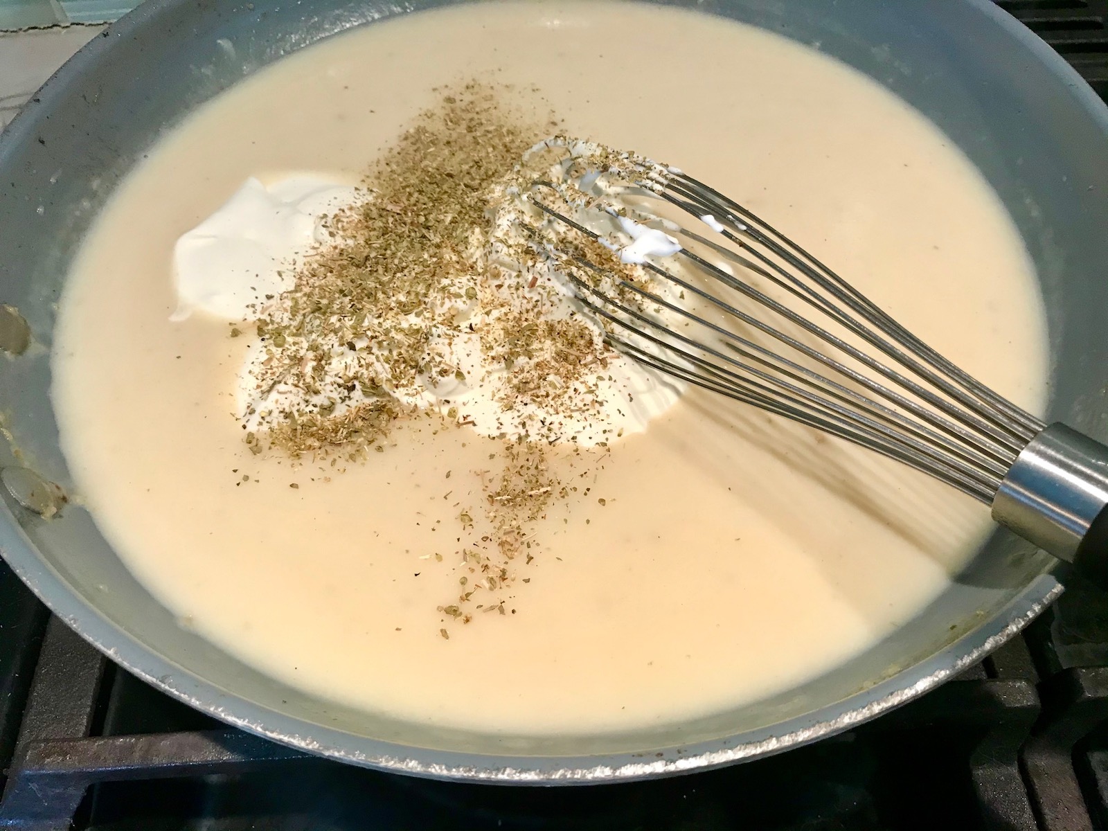 Whisking sour cream, oregano, salt, and pepper into sauce in pan for Cheesy Hamburger Potato Casserole. It's an easy, yummy, and cozy weeknight family dinner.