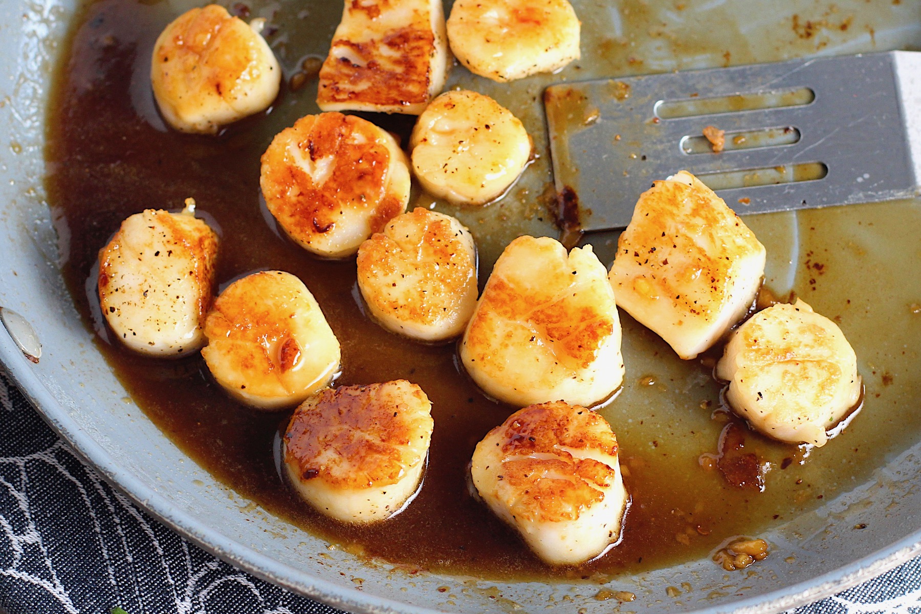 Glazed Pan Seared Scallops with Garlic and Honey in a pan with spatula.