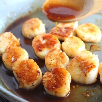 Wood spoon drizzling glaze on Glazed Pan Seared Scallops with Garlic and Honey in a pan with spatula.