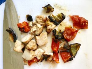 Grilled chicken, green peppers, tomatoes, and onions cut into pieces on a cutting board for Grilled Teriyaki Chicken Salad..