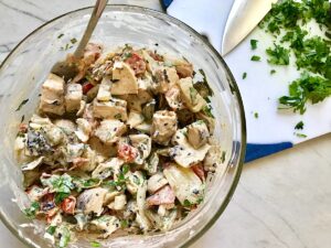 Grilled Teriyaki Chicken Salad in a mixing bowl with spoon and cilantro cut on cutting board on the side with knife.