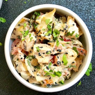 Grilled Teriyaki Chicken Salad in a bowl on black background with chicken, green peppers, tomatoes, onions, black sesame seeds, and cilantro.