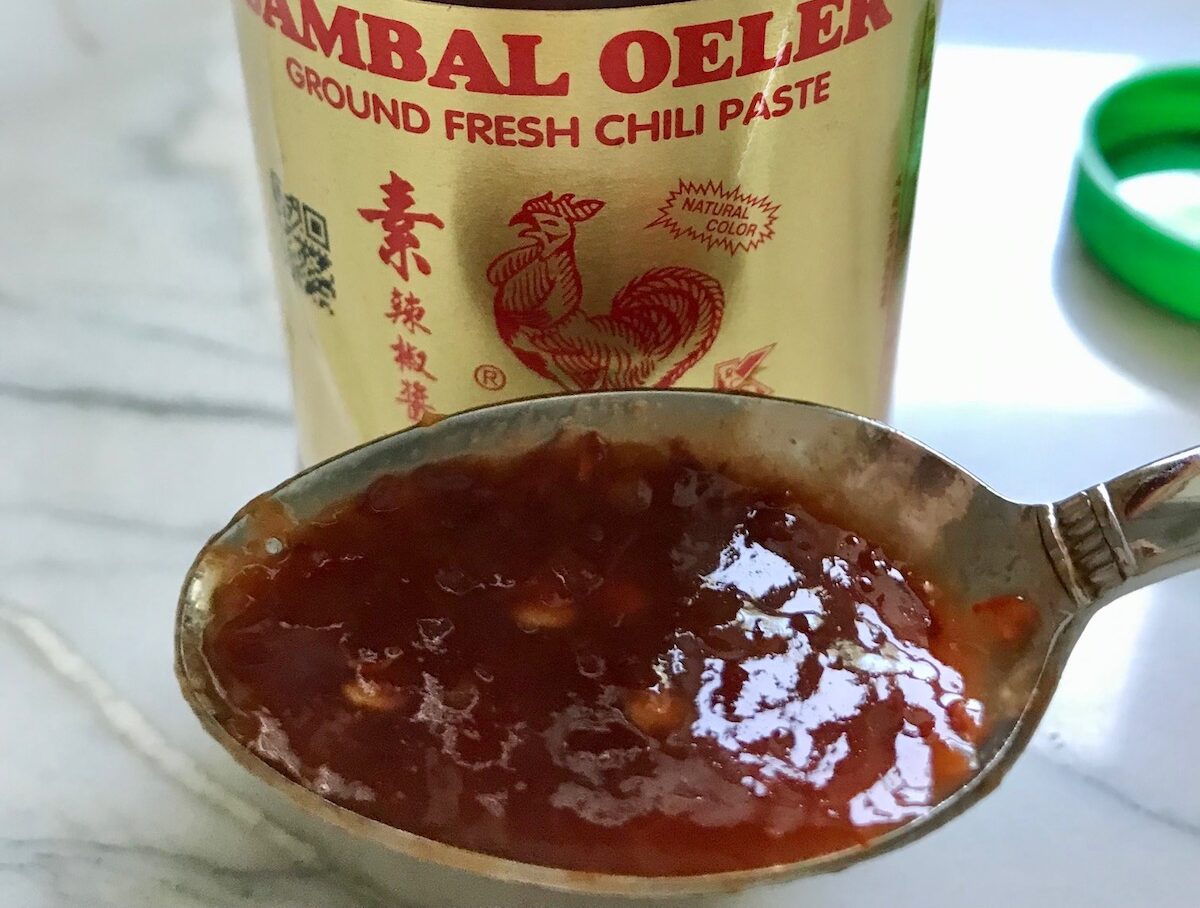 Bottle of Sambal Oelek chili paste with a spoonful in front for Dan Dan Noodle Recipe with Ground Chicken.