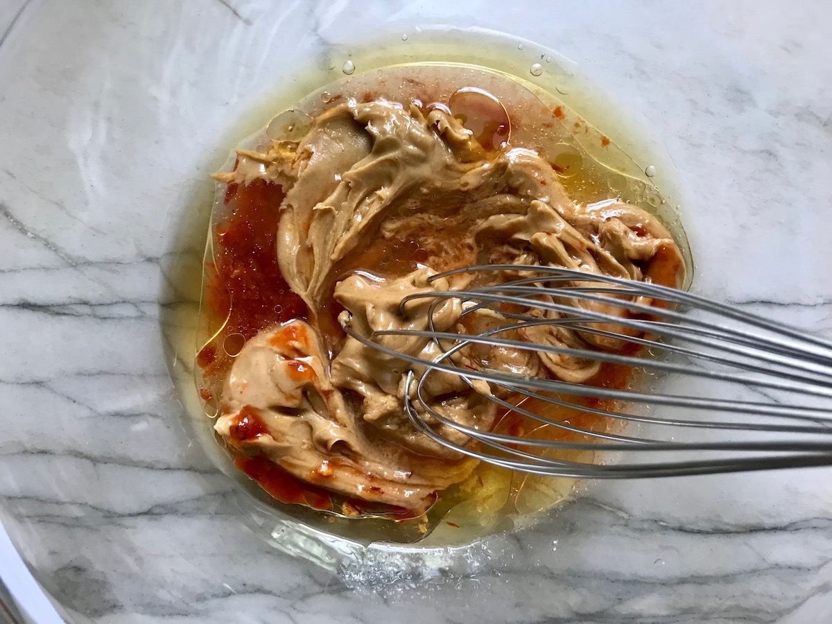 Peanut butter, chili paste, and other ingredients whisking in bowl for Dan Dan Noodle Recipe with Ground Chicken.