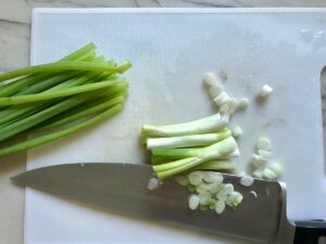 Scallion whites cut and separates from the greens with knife on cutting board for Dan Dan Noodle Recipe with Ground Chicken.