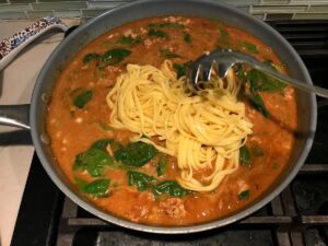 Spoon adding noodles to pan with chicken and sauce for Dan Dan Noodle Recipe with Ground Chicken.
