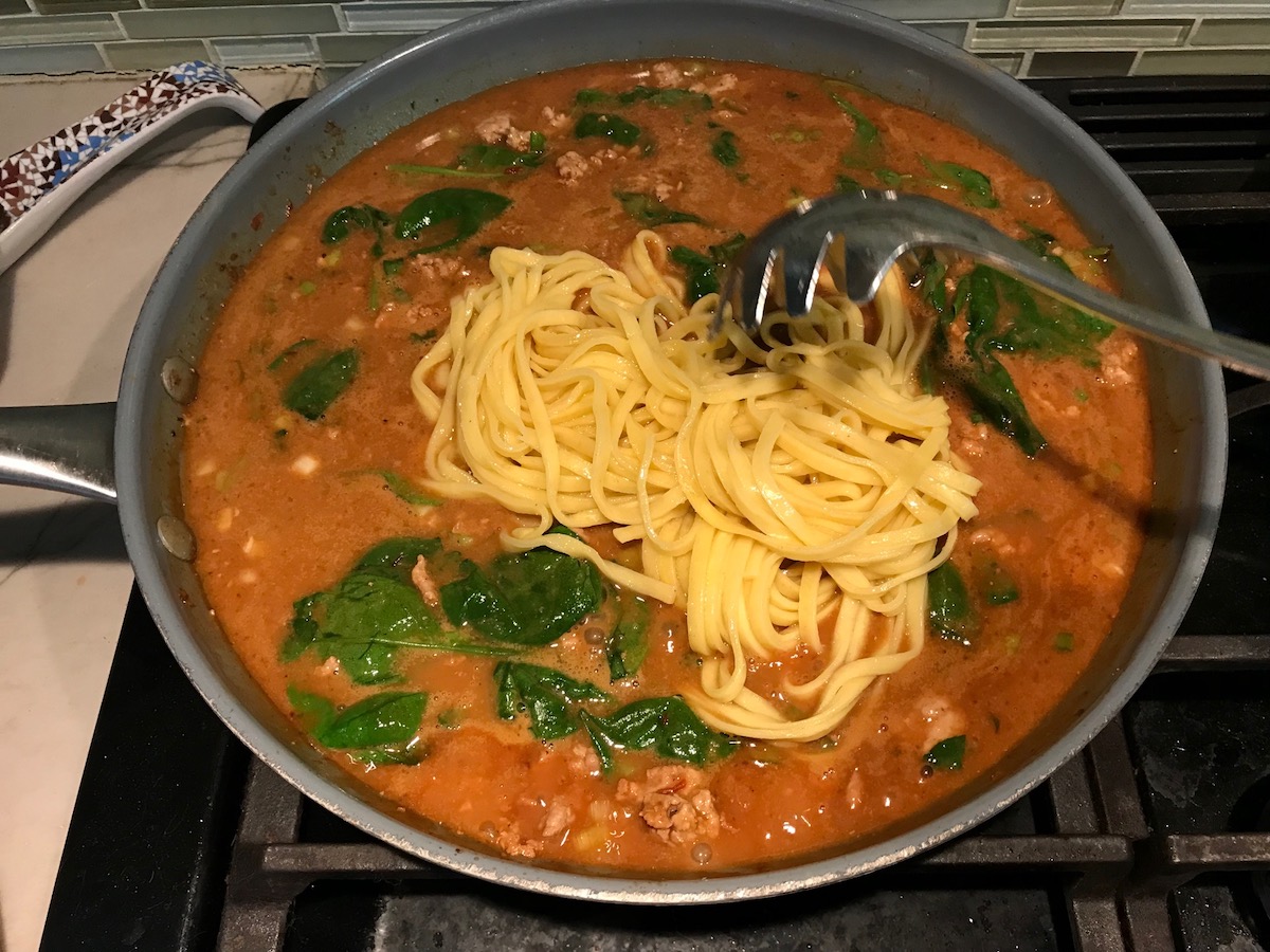 Spoon adding noodles to pan with chicken and sauce for Dan Dan Noodle Recipe with Ground Chicken.