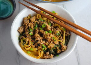 Dan Dan Noodle Recipe with Ground Chicken in a bowl. Chopsticks are sitting on top and scallion slices are on top.