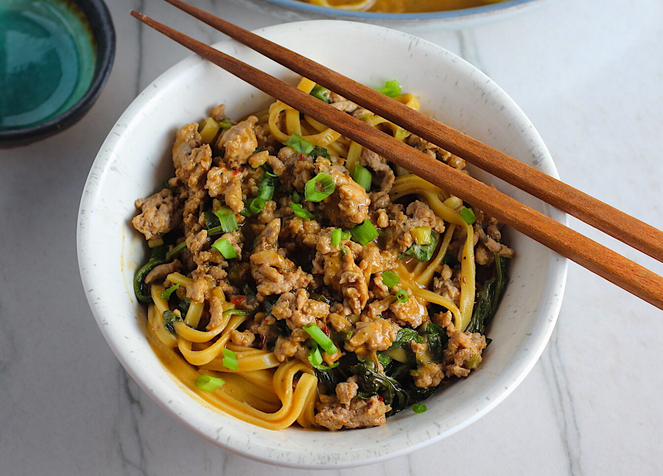 Dan Dan Noodle Recipe with Ground Chicken in a bowl. Chopsticks are sitting on top and scallion slices are on top.