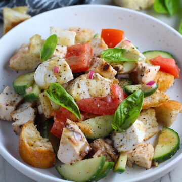 Toasted bread cubes, chicken, tomatoes, cucumber, basil, and mozzarella in a bowl for this Chicken Panzanella Salad Recipe. It's absolutely delicious.