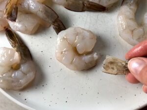 Tail removed from a raw shrimp with more shrimp on the plate for Grilled Shrimp Tacos