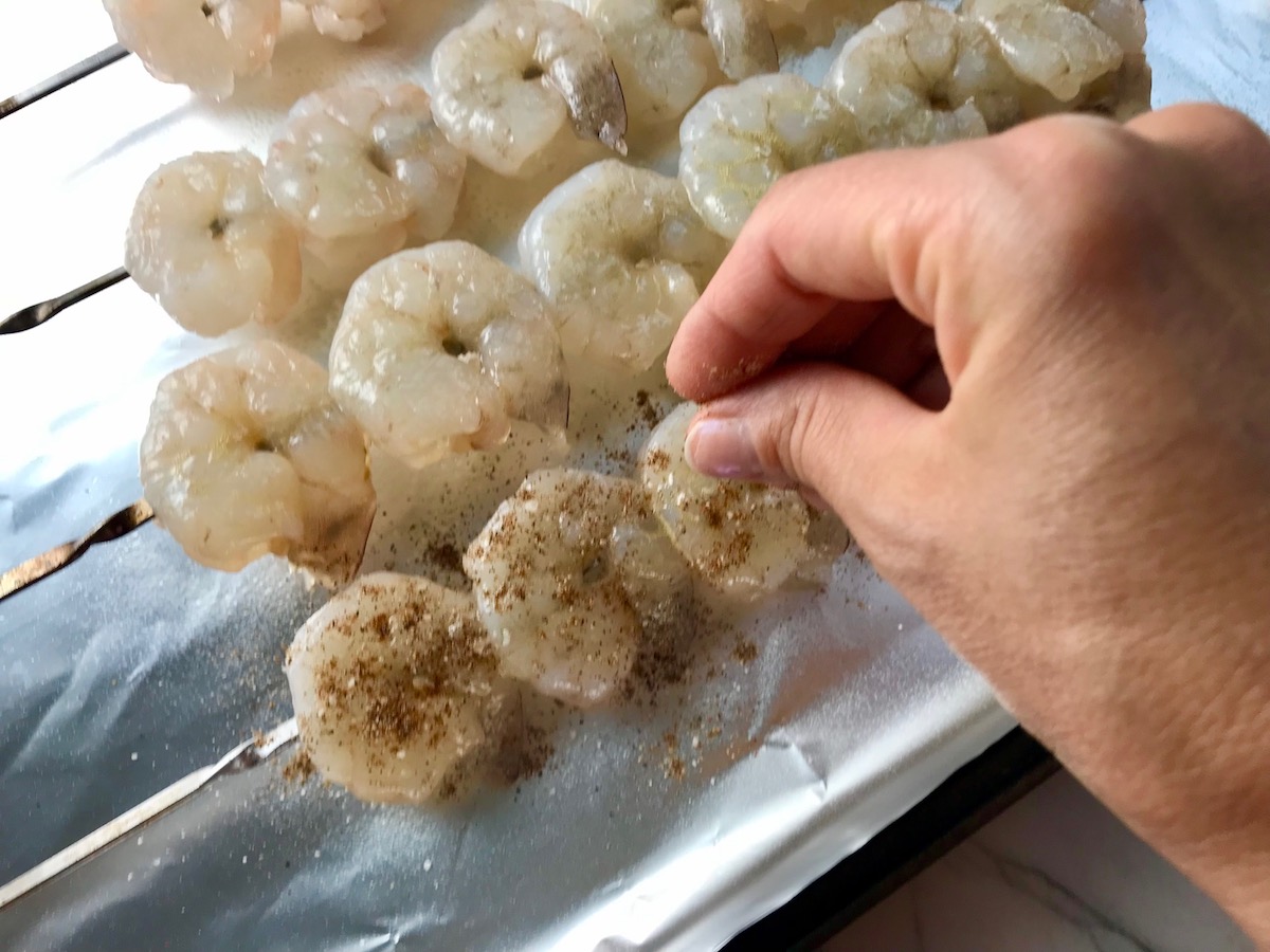 Hand seasoning raw shrimp on skewers for Grilled Shrimp Tacos