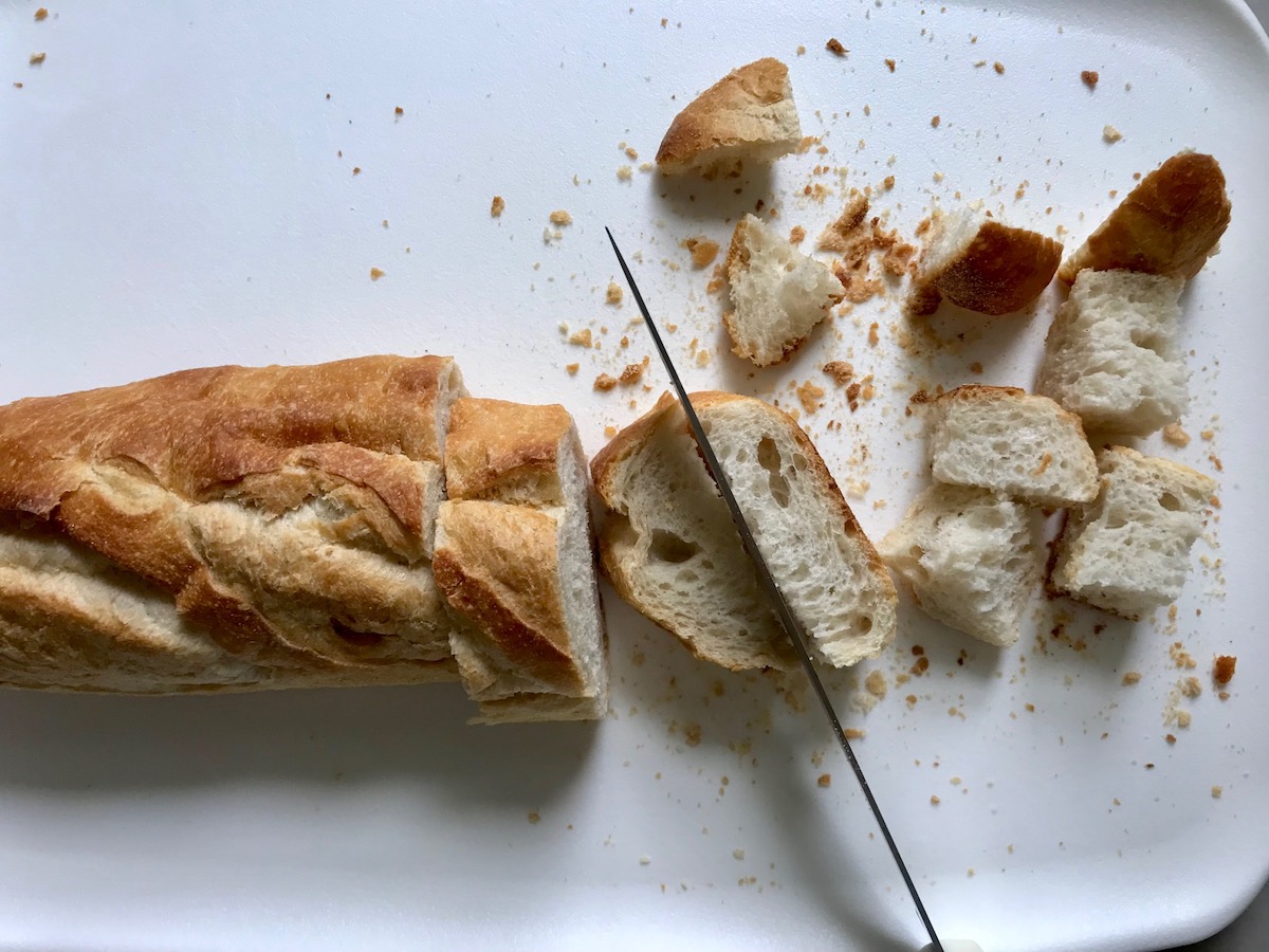 Knife cutting crusty bread into cubes for this Chicken Panzanella Salad Recipe. It's absolutely delicious.