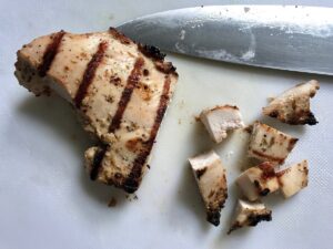 Half grilled chicken breast cut into cubes with knife sitting next to it on cutting board for this Chicken Panzanella Salad Recipe. It's absolutely delicious.