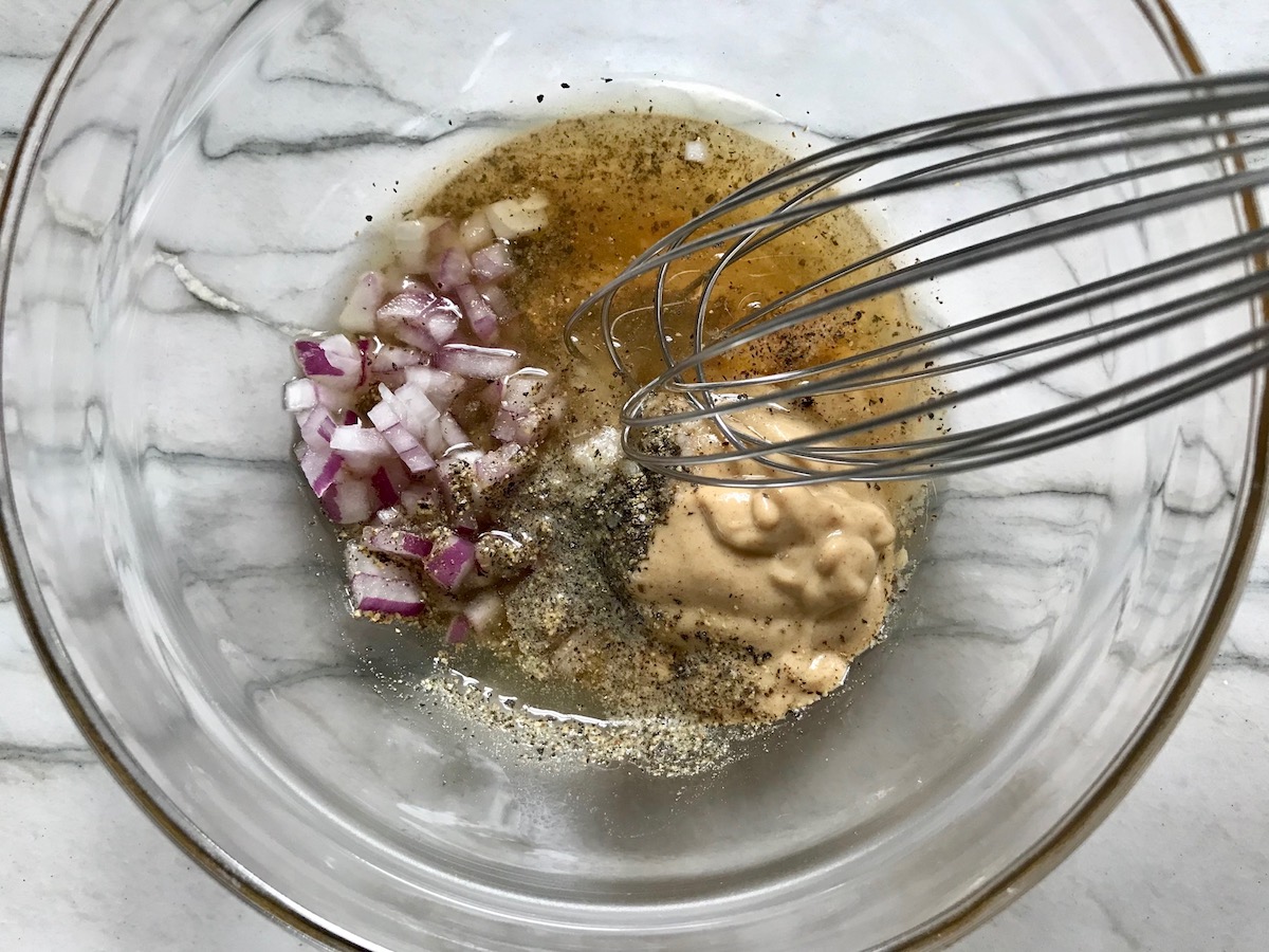 Whisk mixing red onions, dijon, honey, oil, salt, and pepper in a bowl for this Chicken Panzanella Salad Recipe. It's absolutely delicious.